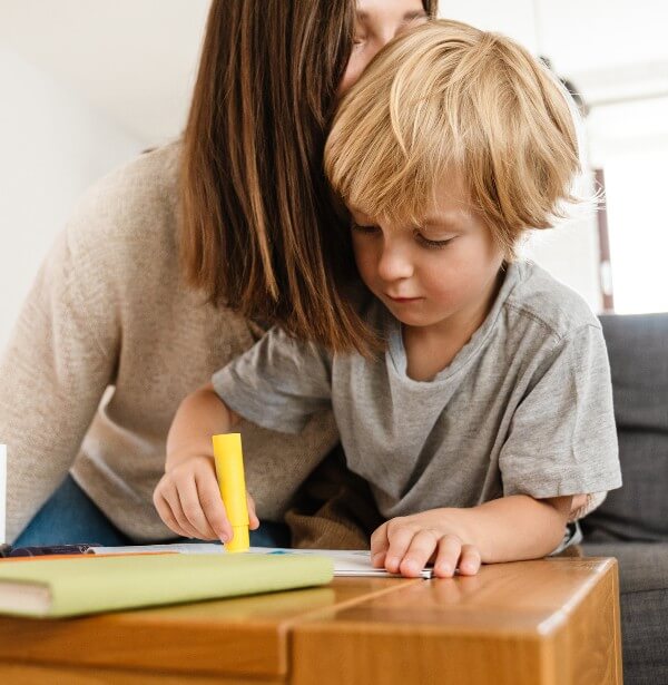 mom kissing son on the head while he colors