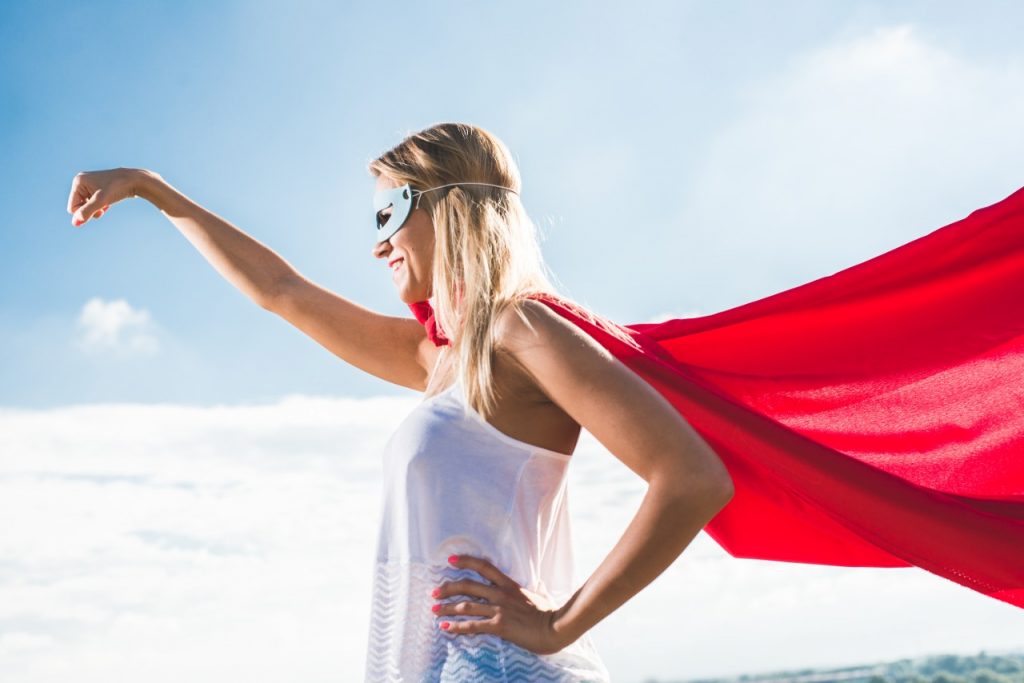 happy woman dressed in superhero cape and mask