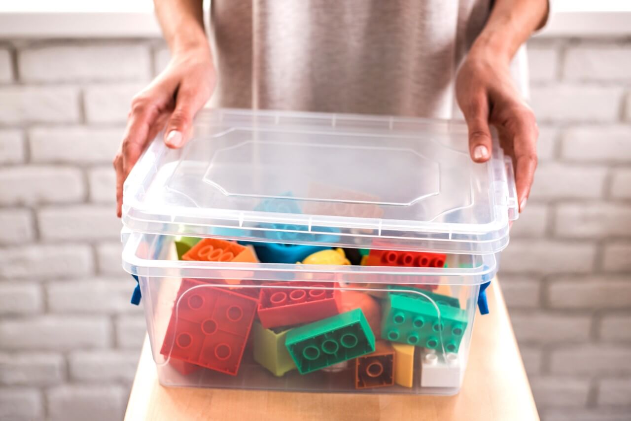 woman putting away toys in plastic bucket