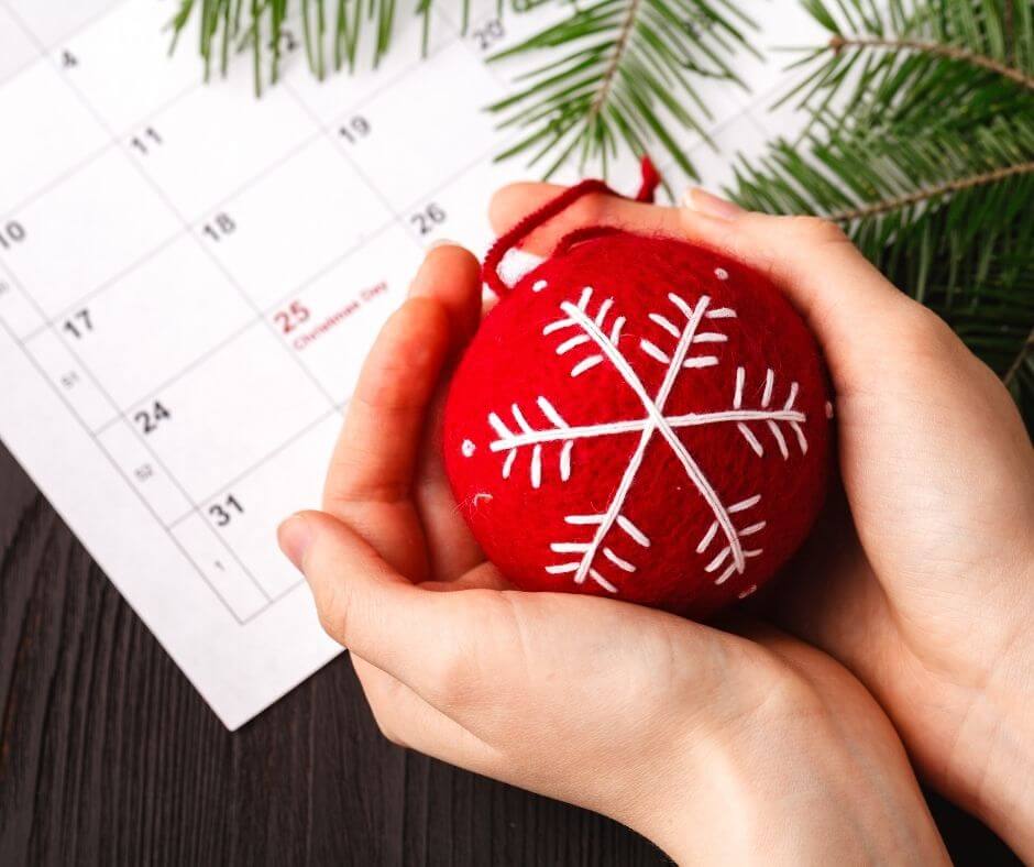 hands holding ornament over a calendar showing christmas day