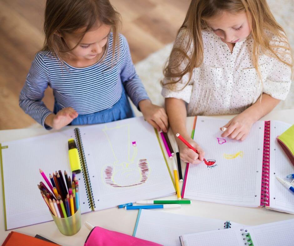 Two girls drawing with markers on notebooks