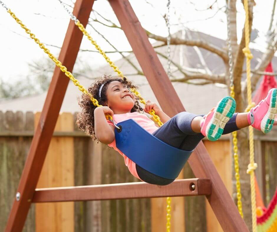 girl swinging on a backyard wooden swing set