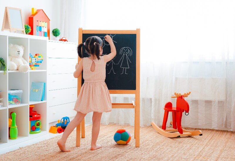 Young girl drawing on a chalkboard in a clean playroom