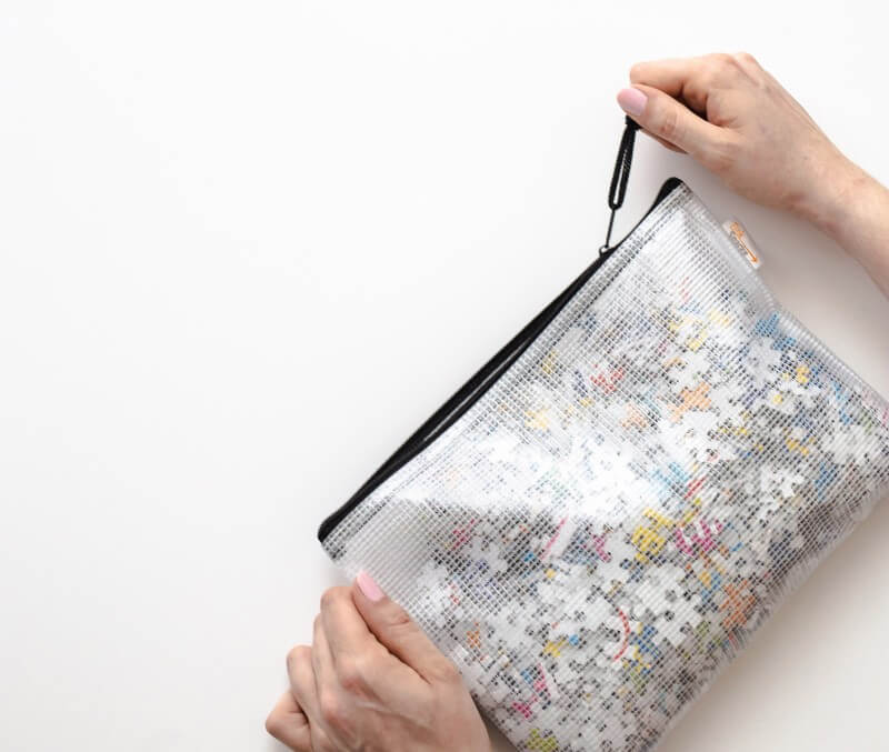 Woman closing translucent zipper pouch that has puzzle pieces inside